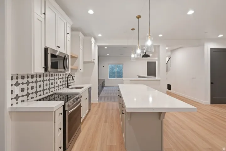 Contemporary kitchen featuring white shaker cabinetry, patterned tile backsplash, stainless steel appliances, and a central island with a light-toned countertop