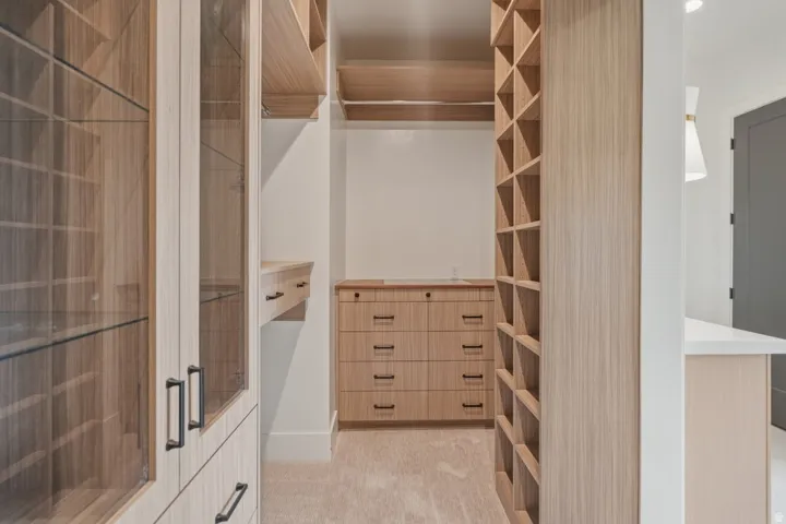 Custom closet system featuring light wood-finish cabinetry, integrated shelving, and glass-front display cabinets