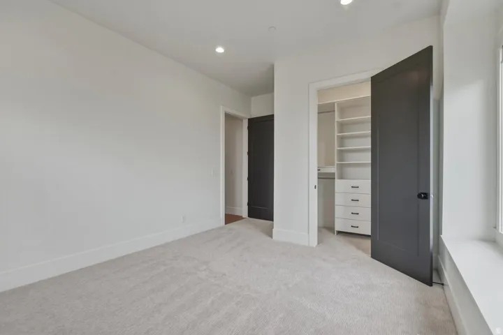 Carpeted room featuring a built-in closet system with shelving and drawers, recessed lighting, and a dark-paneled door