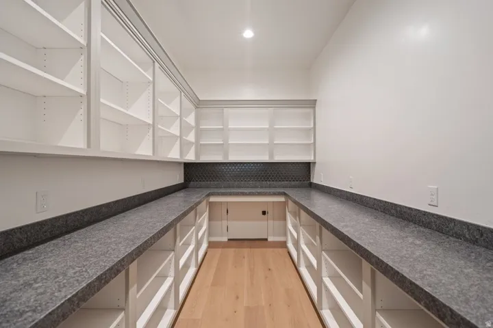 Expansive pantry featuring extensive built-in shelving, dark-toned countertops, a geometric tile backsplash, recessed lighting, and wood-finish flooring