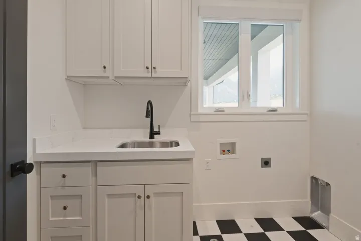 Laundry area featuring white cabinetry, a stainless steel sink with a matte black gooseneck faucet, light-colored countertops, and black and white checkerboard flooring