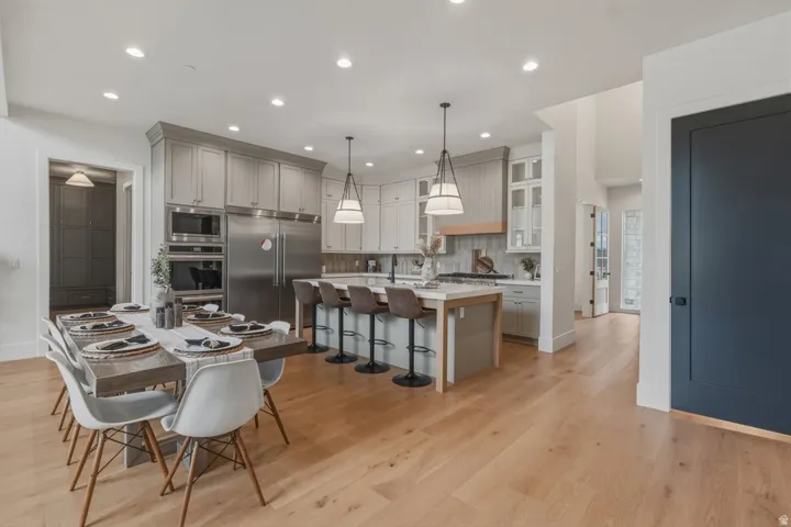 Open-concept kitchen and dining area featuring light wood-finish flooring, a kitchen island with pendant lighting, stainless steel appliances, and shaker-style cabinetry