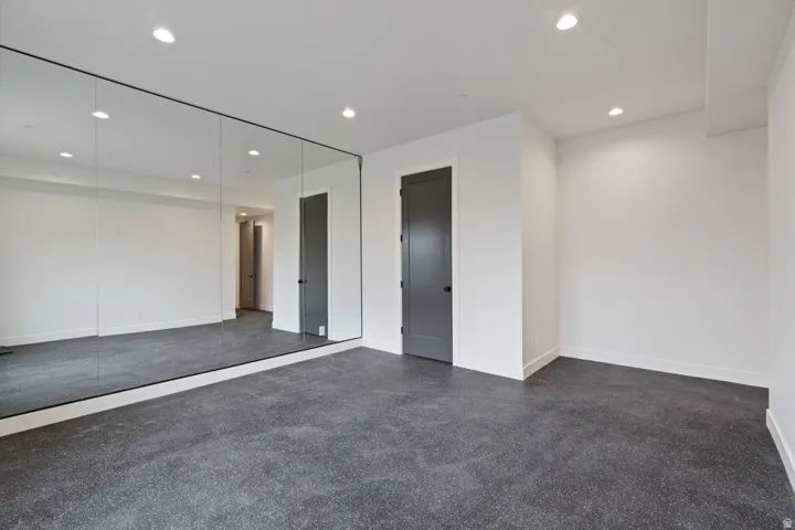 Interior space featuring a full-wall mirror, recessed lighting, white walls, dark paneled door with round black hardware, and dark speckled flooring