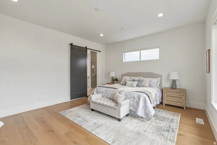 Bedroom featuring wood-finish flooring, recessed lighting, and a dark gray barn door