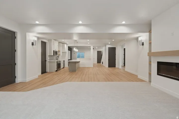 Open-concept living space featuring light wood-finish flooring, recessed lighting, a built-in fireplace with a light wood mantel, and a kitchen with white cabinetry and a central island