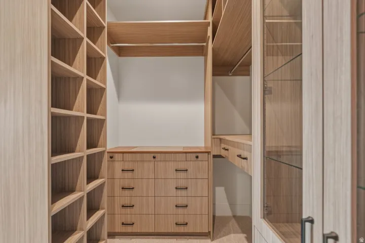 Custom closet system featuring light wood-finish cabinetry, integrated shelving, multiple drawers, and glass-front display cabinets