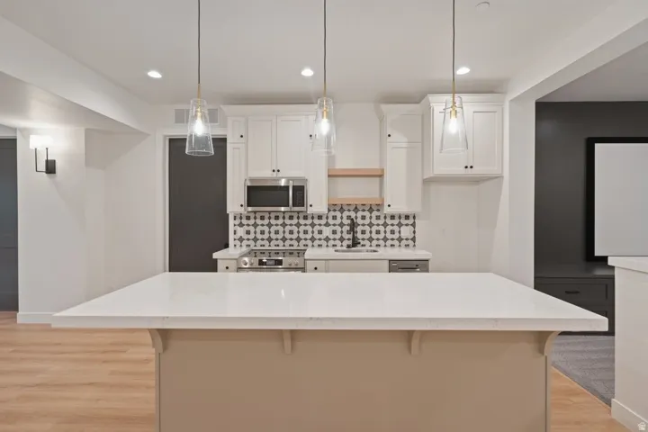 Kitchenette featuring white cabinetry, patterned tile backsplash, stainless steel appliances, and a substantial center island with a light-toned countertop