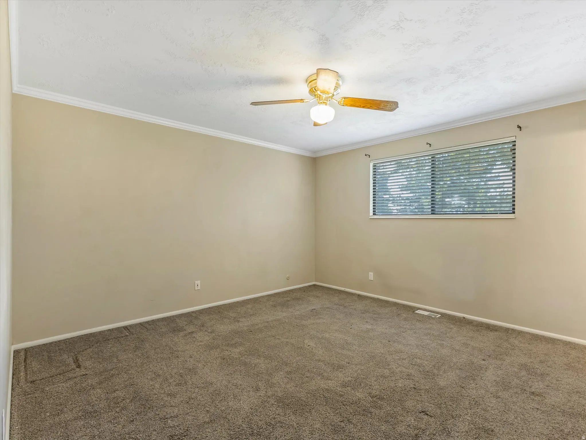 Room featuring neutral wall paint, crown molding, a window with blinds, and a ceiling fan with light fixture