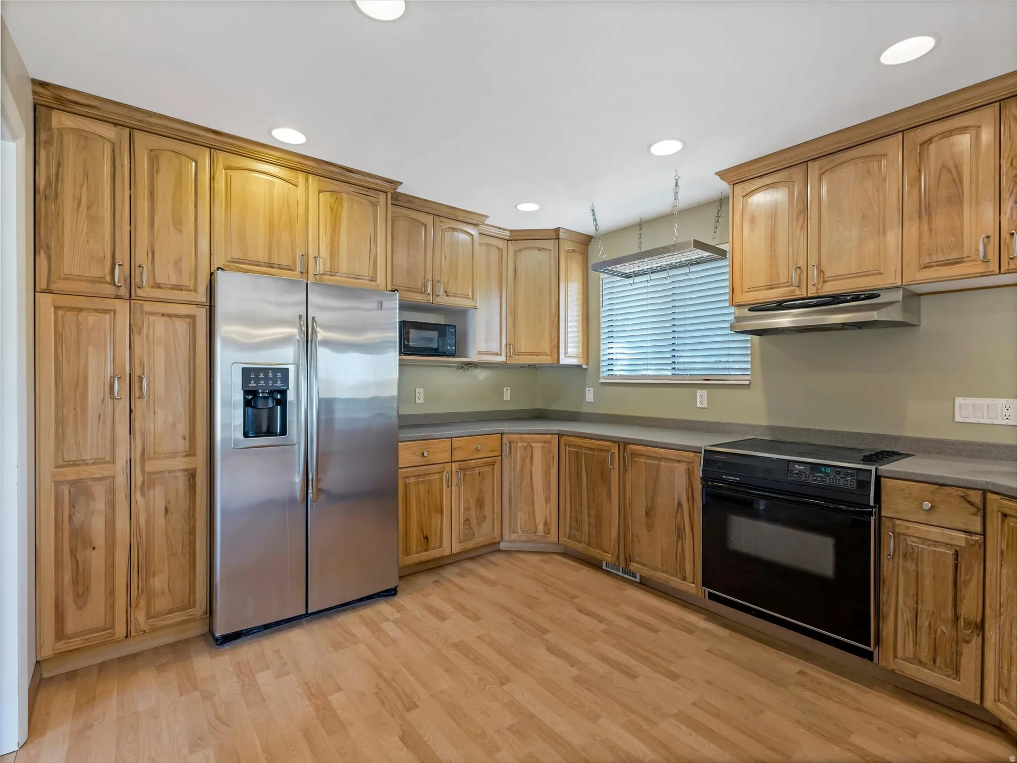 Kitchen featuring extensive wood cabinetry, wood-finish flooring, a stainless steel side-by-side refrigerator, built-in black oven, and recessed lighting