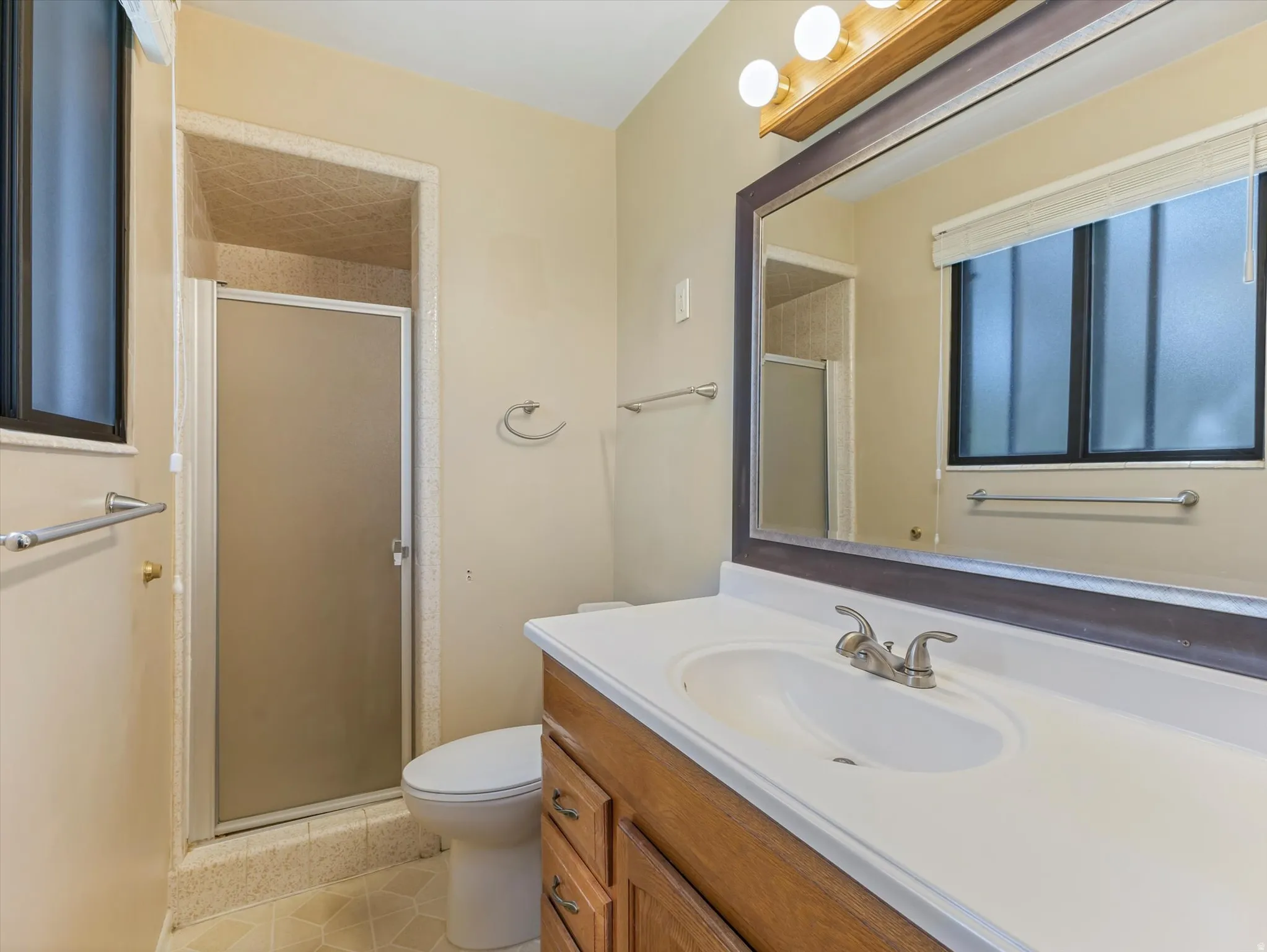 Bathroom featuring a vanity with wood-finish cabinetry, a single basin sink, a large wall-mounted mirror, and shower