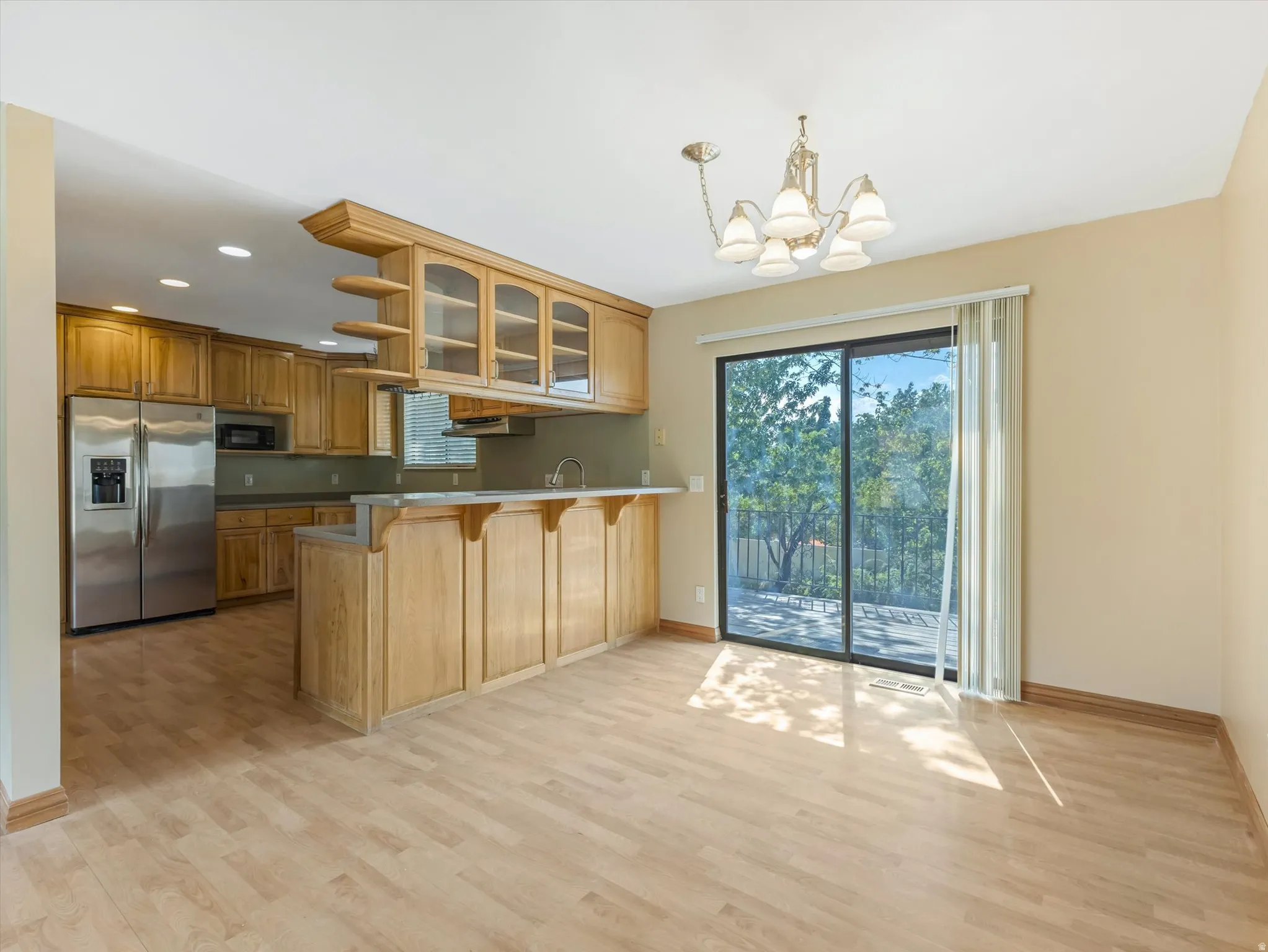 Open-concept living space featuring wood-finish flooring, a kitchen with stainless steel appliances, and wood cabinetry with glass-front upper cabinets