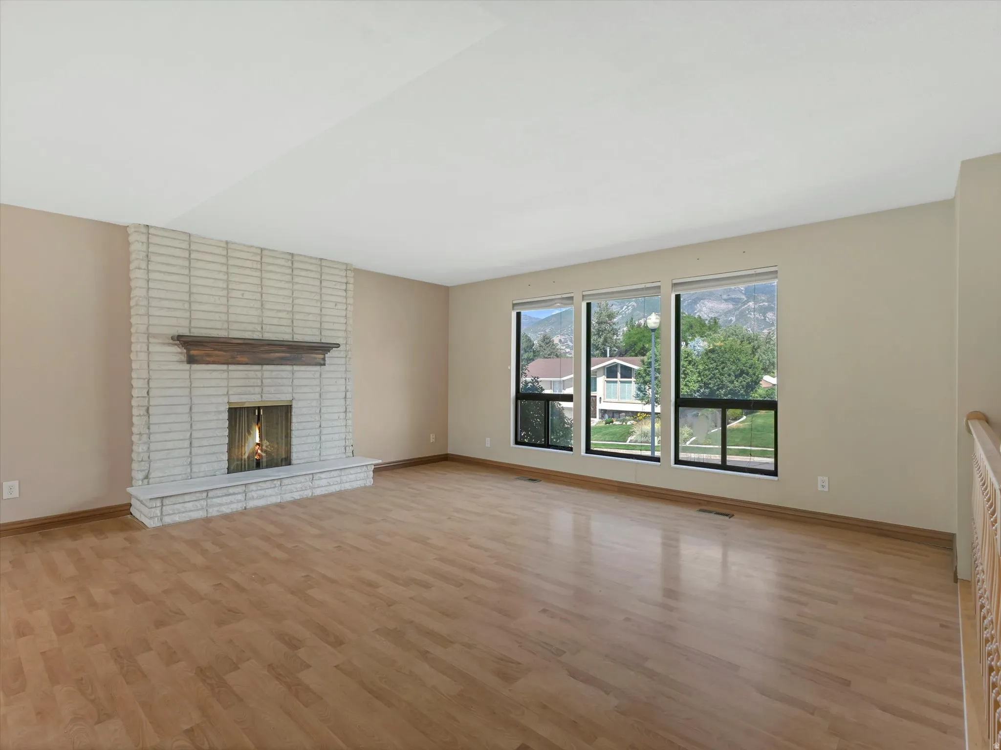 Living area featuring a brick fireplace with a wood mantle, wood-finish flooring, and large windows