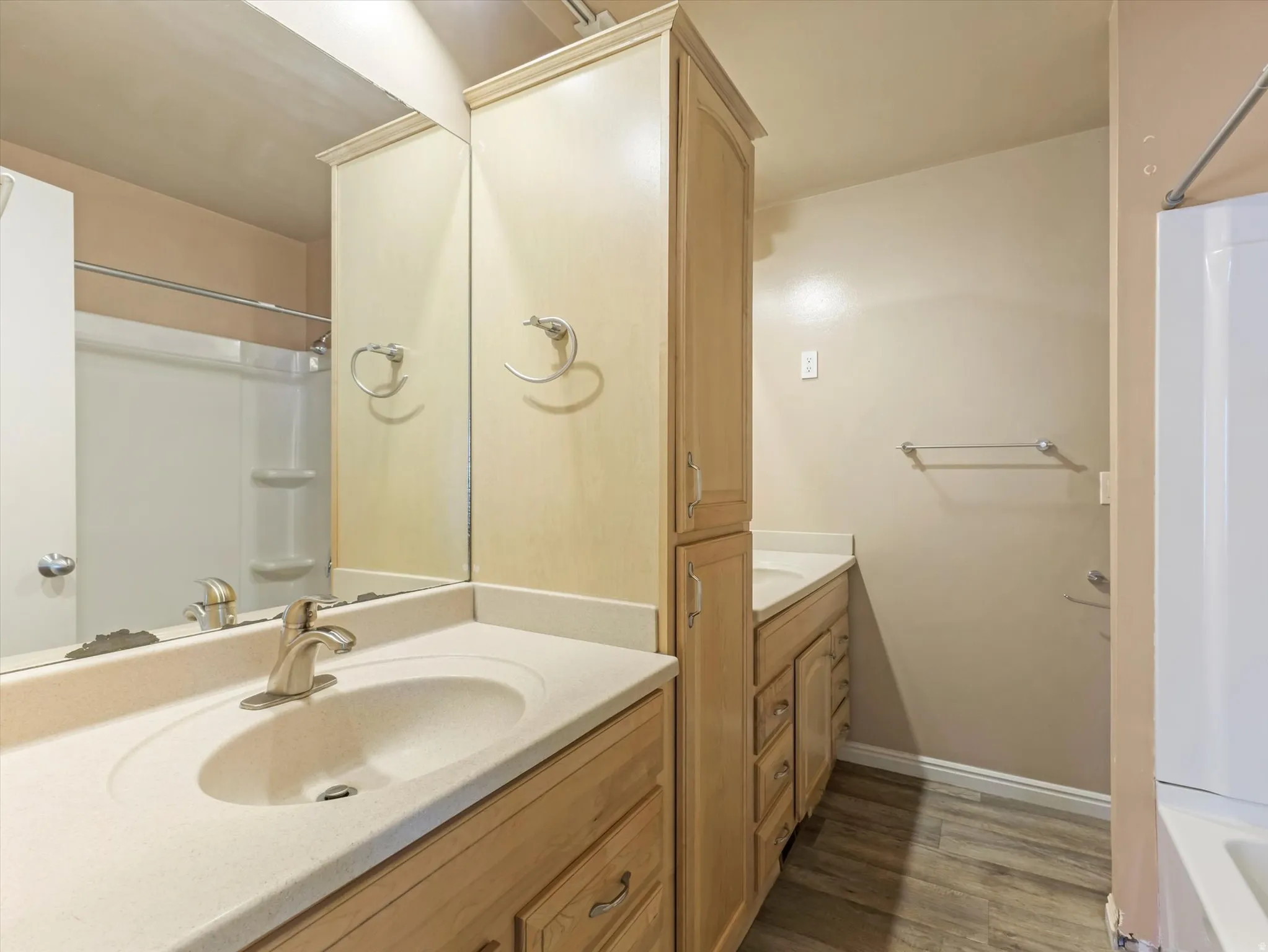 Bathroom featuring dual vanity areas with light wood-finish cabinetry, integrated sinks, and brushed nickel faucets