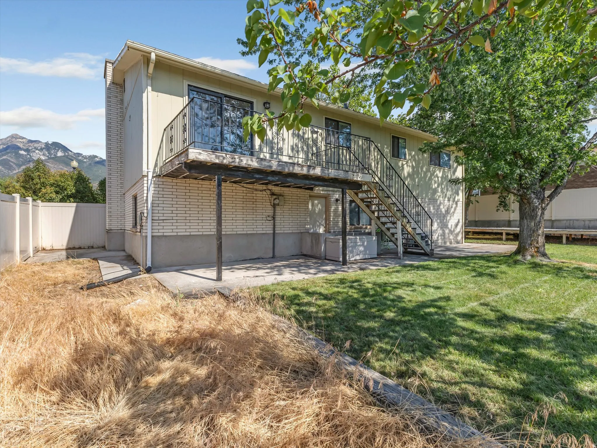 Rear exterior featuring a second-story balcony with metal railings, an exterior staircase, and a ground-level patio