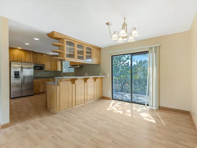Open-concept living space featuring wood-finish flooring, a kitchen with stainless steel appliances, and wood cabinetry with glass-front upper cabinets