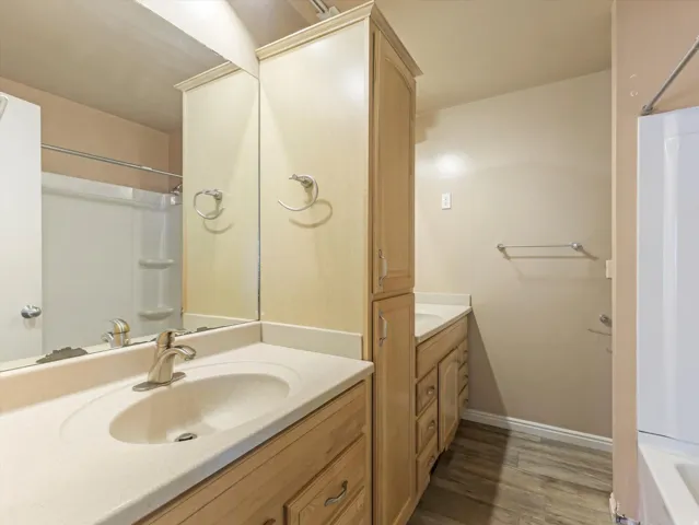 Bathroom featuring dual vanity areas with light wood-finish cabinetry, integrated sinks, and brushed nickel faucets