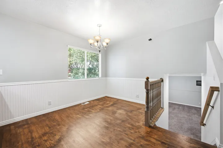 Room featuring wood-finish flooring, white beadboard wainscoting, and a window with blinds