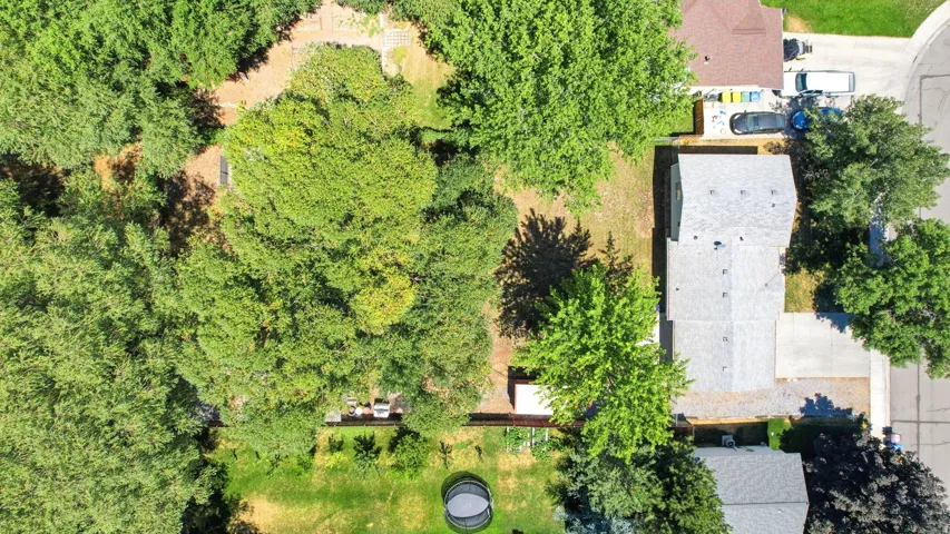 Aerial view showcasing a residential property with a shingled roof and surrounding mature trees
