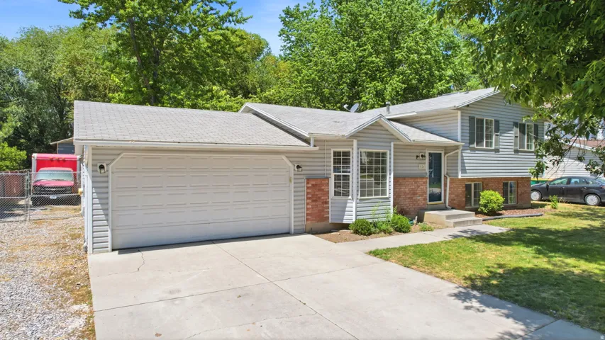 Split-level home featuring light gray siding with brick accents and a concrete driveway