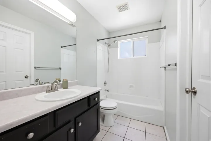 Full bathroom featuring a dark vanity with a light-colored countertop, an integrated sink with brushed nickel fixtures, a tub-shower combination with a window, and white tile flooring