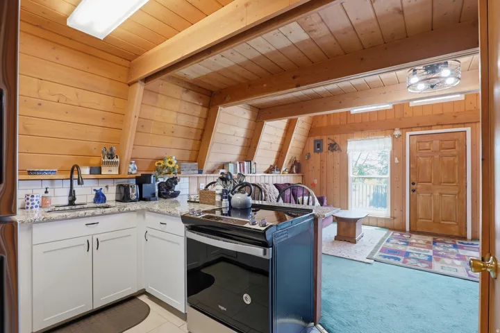 Open-concept kitchen and living area featuring wood-paneled walls and ceiling beams