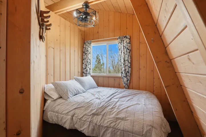 Wood-paneled room featuring an angled ceiling, a centered window, and an exposed structural beam