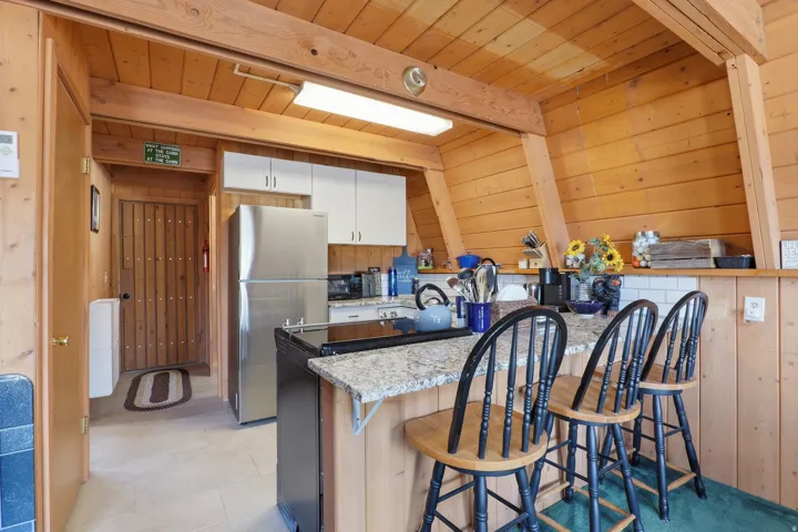 Kitchen featuring wood-paneled walls and ceiling, a breakfast bar with granite-finish countertop, white tile backsplash, and stainless steel appliances