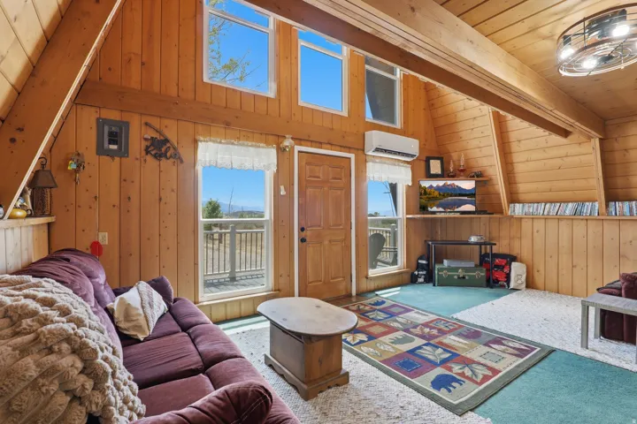 Vaulted ceiling with exposed wood beams, plank wood wall finishes, a wood-panel door, multiple windows, and a ceiling fan