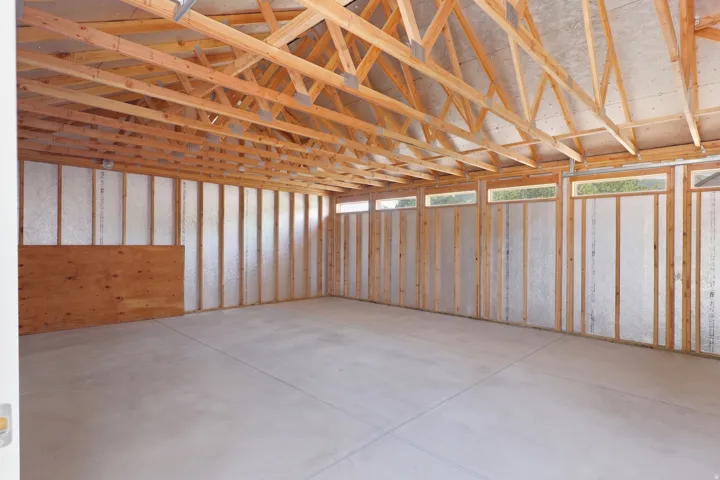 Spacious interior framing featuring exposed wood trusses, upper transom windows, concrete flooring, and insulated wall sheathing