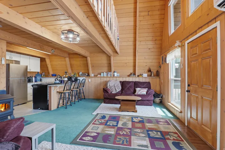 Vaulted wood-paneled living space featuring exposed beams, a wood-burning stove, and a breakfast bar with seating