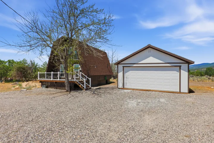 A-frame residence featuring a brown shingle roof, an elevated porch with white railings, and an accompanying detached garage with a white panel door