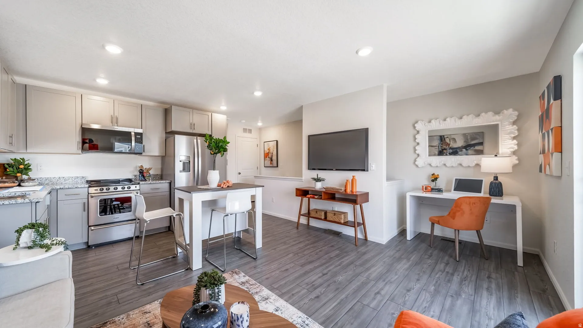 Open-concept living area featuring a kitchen with light gray cabinetry, stainless steel appliances, and stone countertops