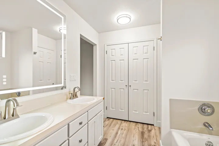 Dual vanity with white cabinetry and integrated sinks, illuminated by an LED-framed mirror