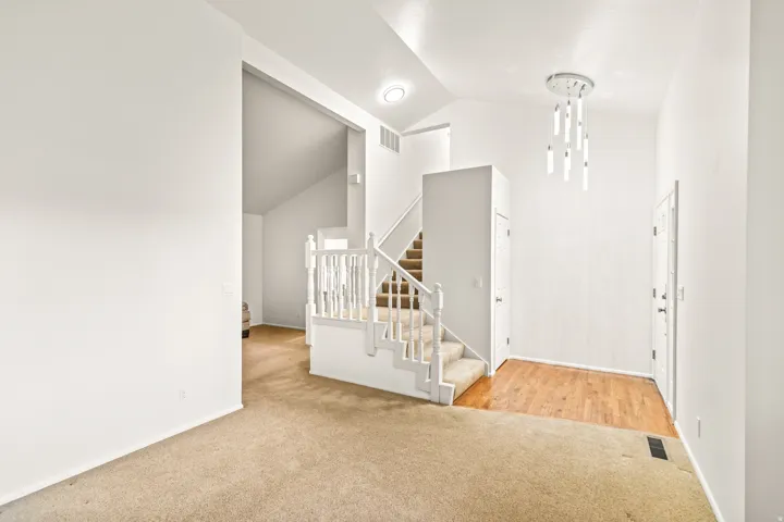 Entryway featuring a modern multi-pendant chandelier, wood-finish flooring, and a carpeted staircase with white balusters