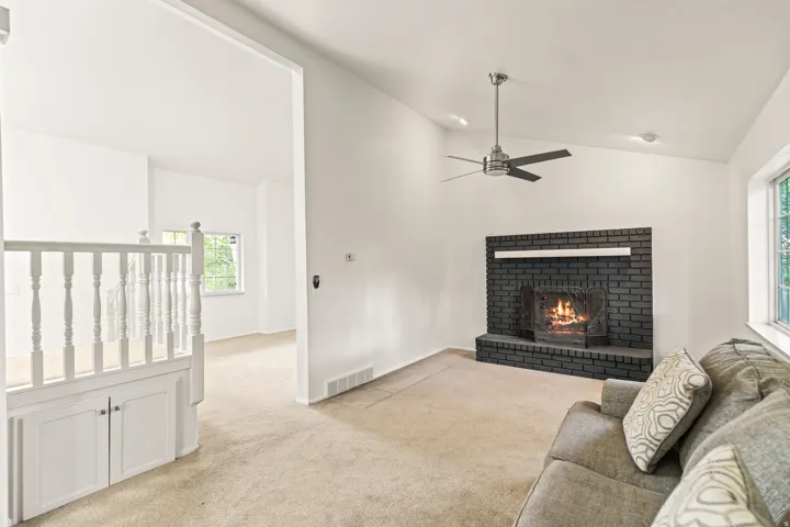 Living area featuring a floor-to-ceiling black brick fireplace with a white mantel, vaulted ceilings, a ceiling fan with brushed nickel accents, and a large window