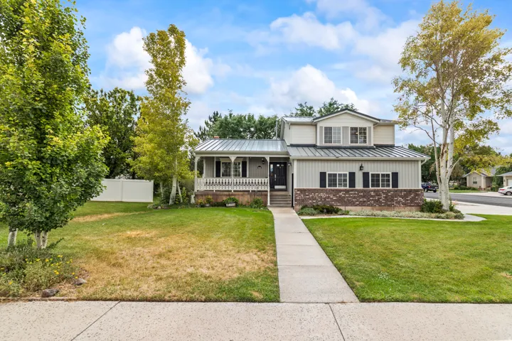Two-story residence featuring a metal roof, a covered front porch with white railing, and a brick facade accent