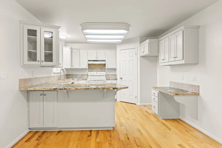 Kitchen featuring white cabinetry, light-toned wood-finish flooring, granite countertops with matching backsplash, and a built-in desk area