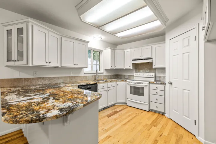 Kitchen featuring light wood-finish flooring, white cabinetry with silver-tone hardware, and a stone-finish countertop