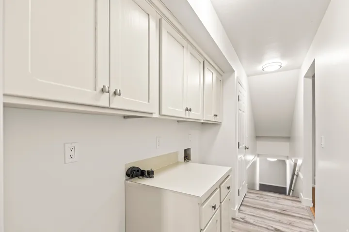 Laundry area featuring white shaker-style cabinetry with brushed nickel hardware, light-toned countertops, and wood-finish flooring