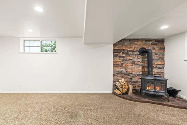 Built-in wood-burning stove with a stone veneer surround, recessed lighting, carpet flooring, and an egress window