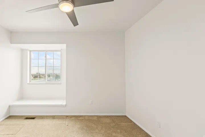 Room featuring a ceiling fan with integrated lighting, a window with gridded panes, a built-in window bench, and light-toned carpeting