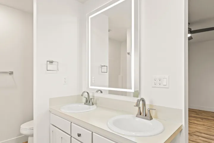 Bright bathroom featuring a dual vanity with white cabinetry, light-toned countertops, and two undermount sinks with brushed nickel fixtures