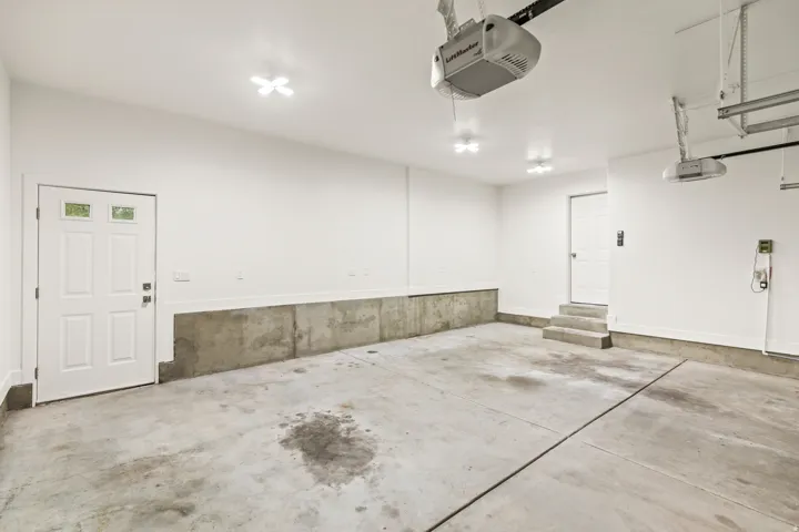 Spacious garage with concrete flooring, bright overhead lighting, two garage door openers, and a white interior door with multiple glass panes