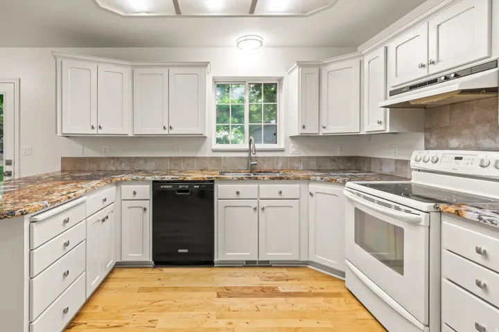 Kitchen featuring white cabinetry, wood-finish flooring, stone countertops, and a tile backsplash