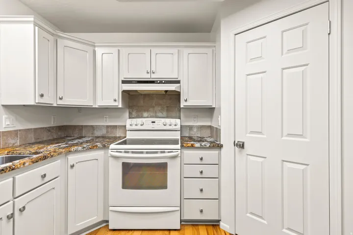 Kitchen featuring white cabinetry with silver hardware, granite-patterned countertops, a tile backsplash, and a white electric range with an overhead microwave