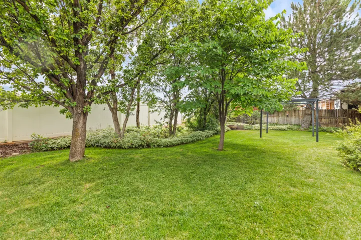 Expansive backyard featuring a lush lawn, mature trees, a white privacy fence, and a metal pergola frame