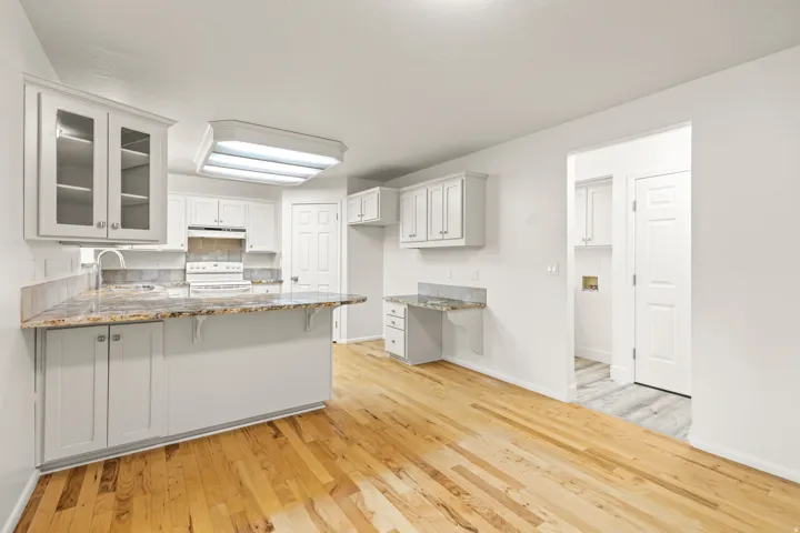Kitchen featuring light wood-finish flooring, white cabinetry, granite-style countertops, and a built-in desk area