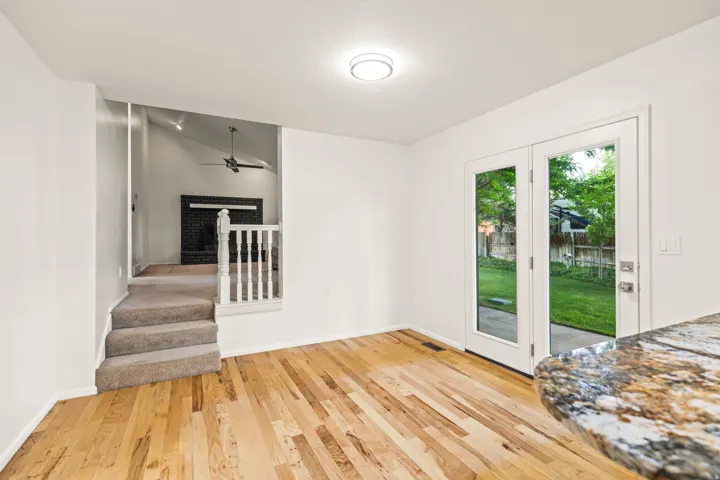 Hardwood flooring extending from a granite-finish countertop to French doors opening onto a green outdoor area
