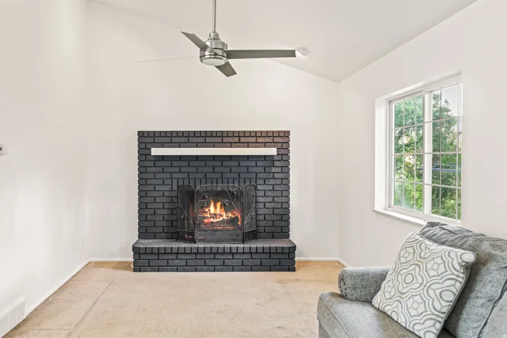 Vaulted ceiling featuring a ceiling fan, black brick fireplace with a white mantel, and a multi-pane window