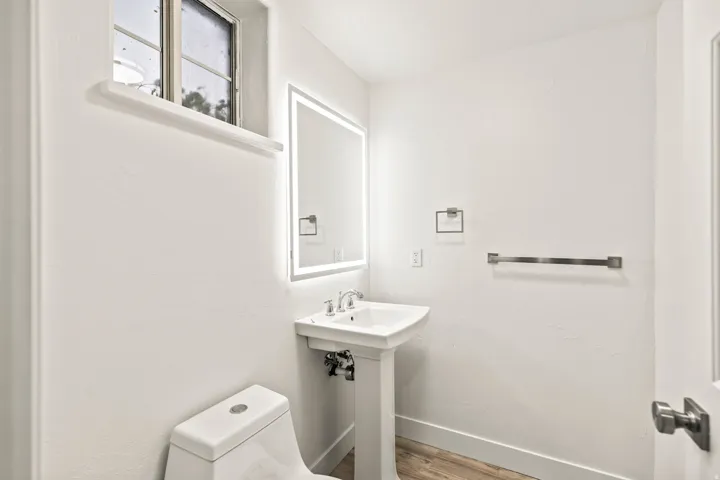 Pedestal sink with chrome faucet, illuminated mirror, and a low-profile toilet